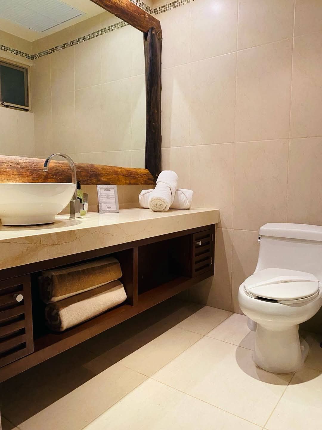 Baño con lavabo sobre un mueble de madera, espejo e inodoro