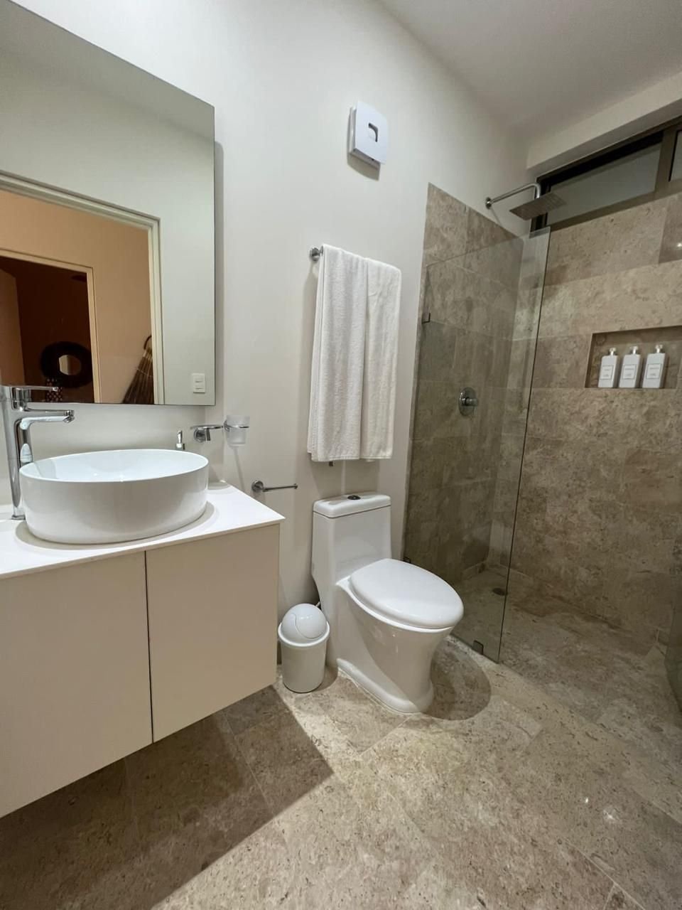 Baño con lavabo blanco, espejo y regadera con cancel de cristal