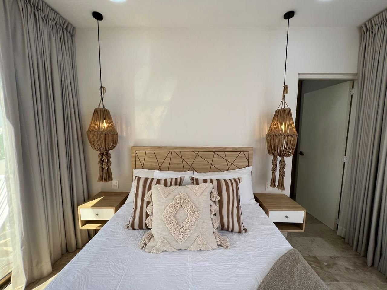Recámara con cama, cortinas y lámparas de macramé junto a la ventana