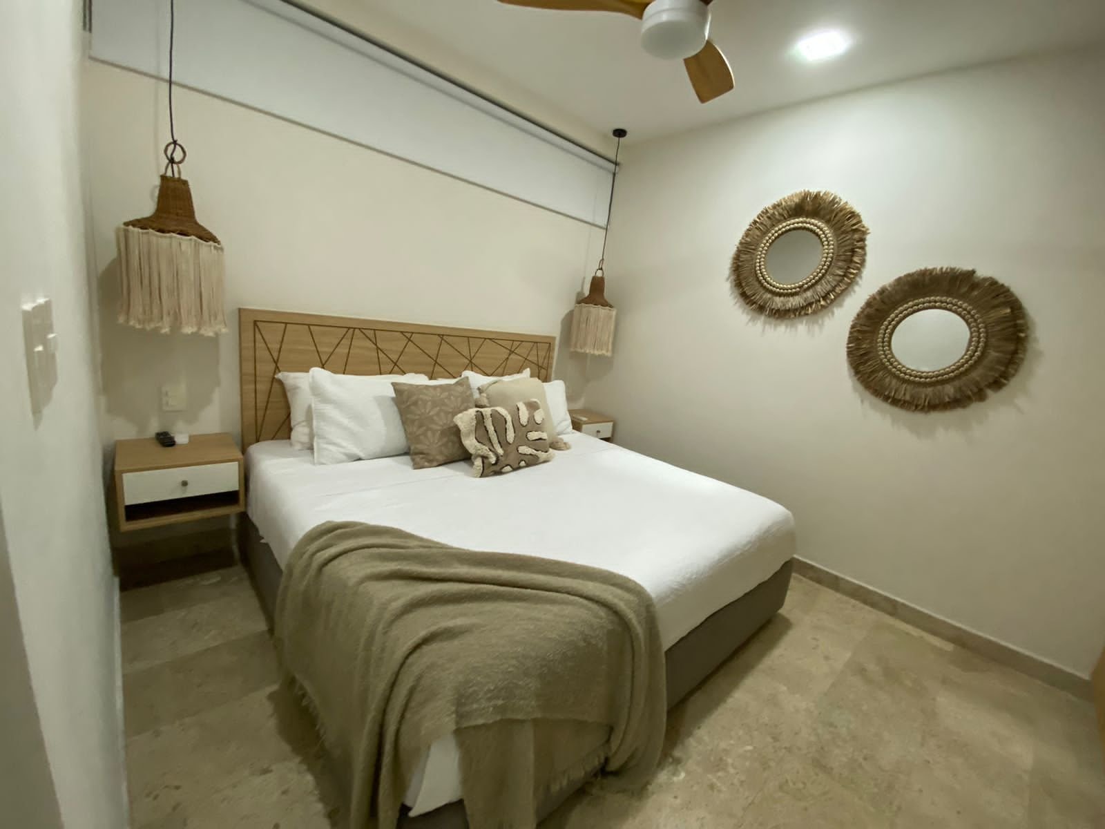 Recámara con cama, cabecera de madera, espejos de palma y ventilador de techo
