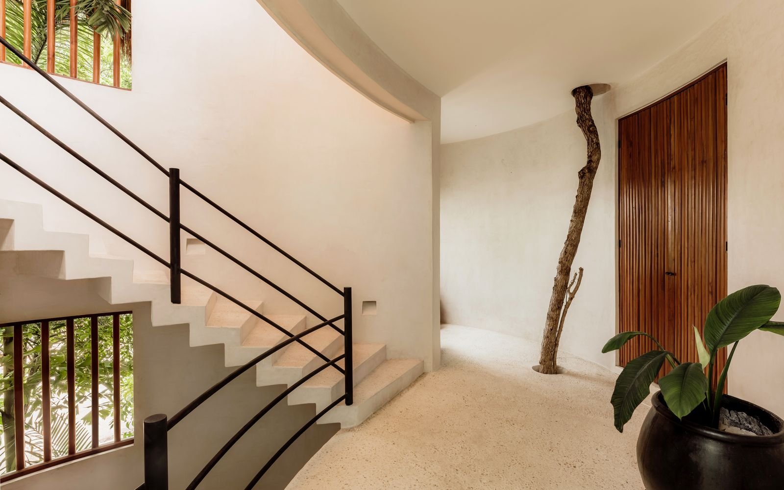 Escalera curva con barandal negro y un tronco en el piso