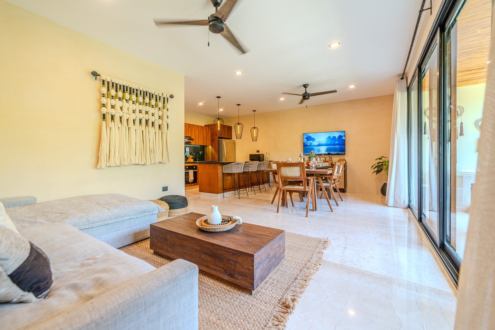 Sala con sofá claro, mesa de madera y cocina abierta en un departamento administrado en Tulum.