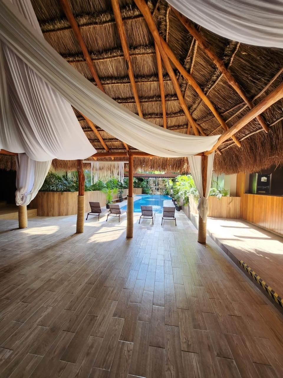 Palapa con techo de palma, cortinas blancas y piso de madera