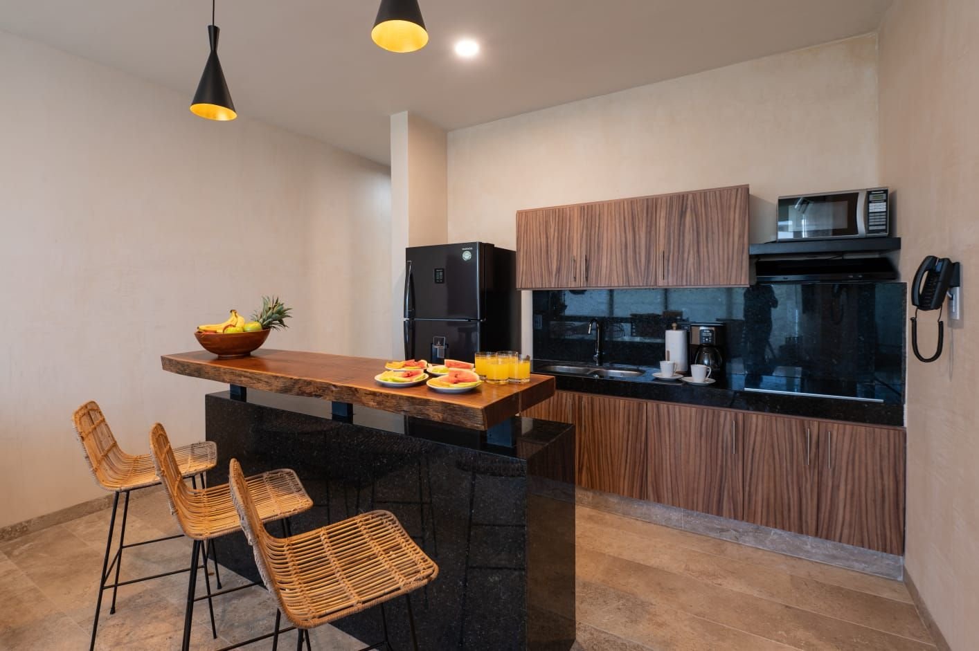 Cocina con barra de madera, bancos de mimbre, refrigerador y microondas